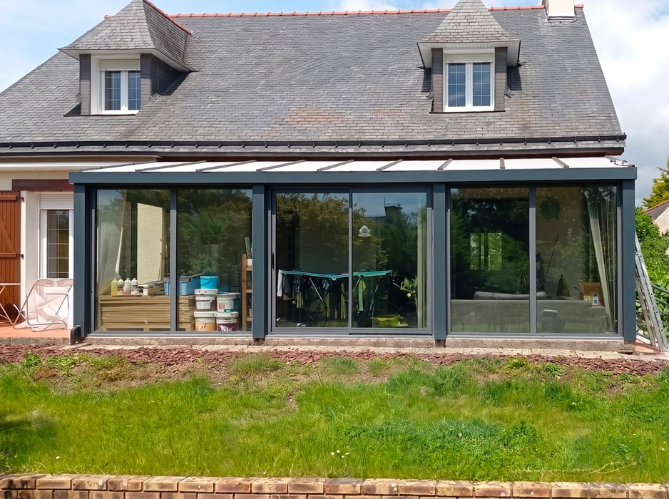Véranda aluminium gris anthracite adossée à une maison en pierre et ardoise
