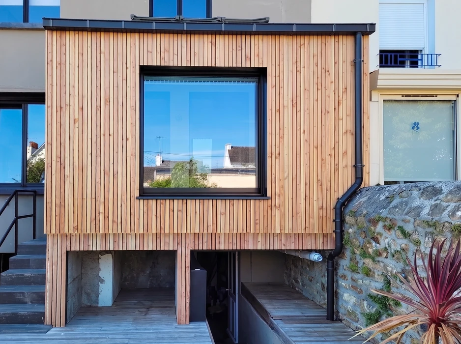 Façade contemporaine d'une extension de maison, bardage en lames de bois verticales en douglas naturel, fenêtre fixe grand format avec cadre aluminium anthracite, vitrage réfléchissant